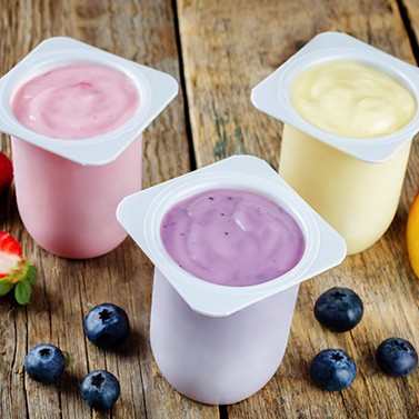 Three flavors of yogurt in containers on wooden surface next to fruits